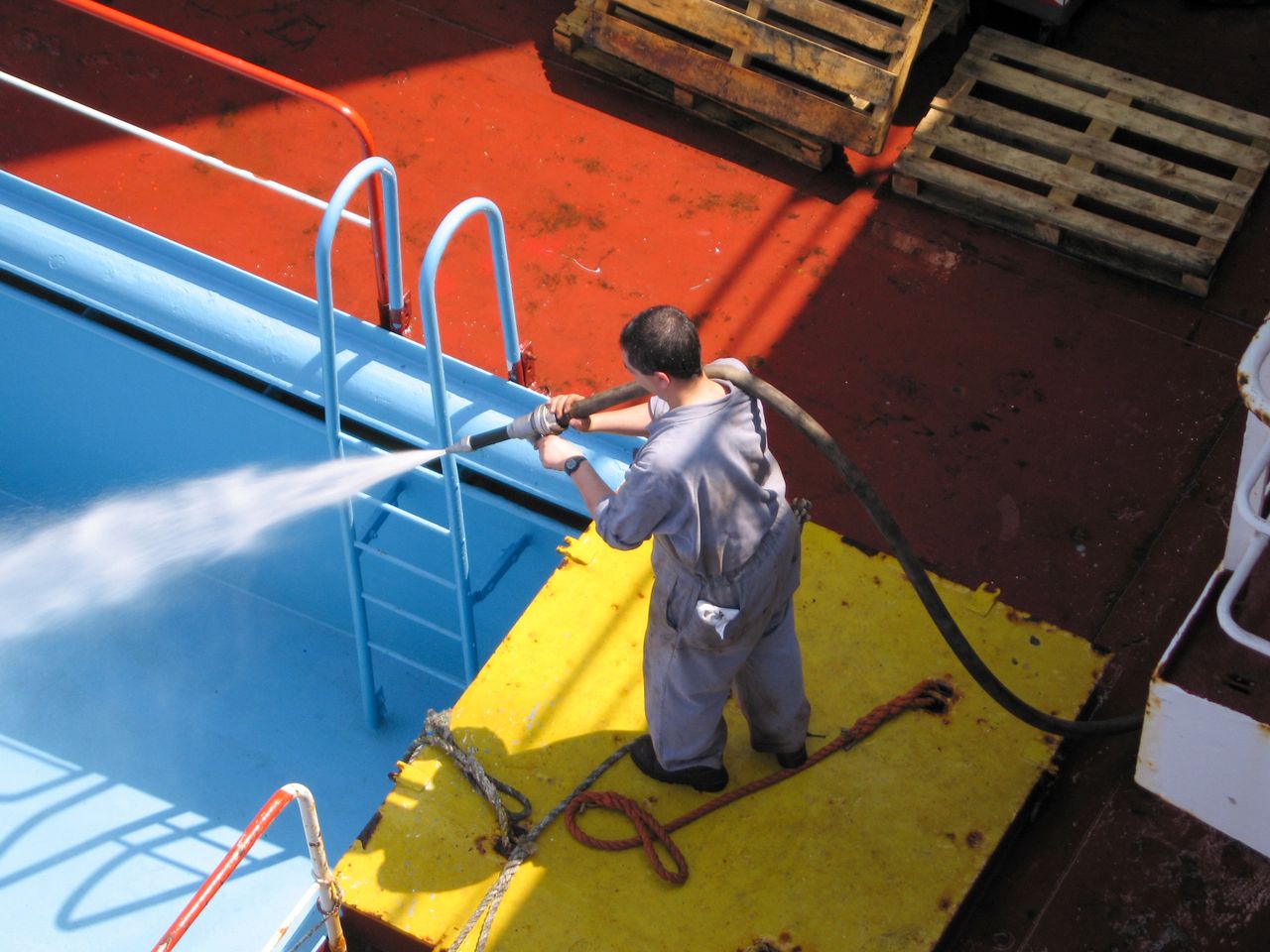 A worker using a high-pressure hose to clean the deck of a ship, showing industrial processes.
